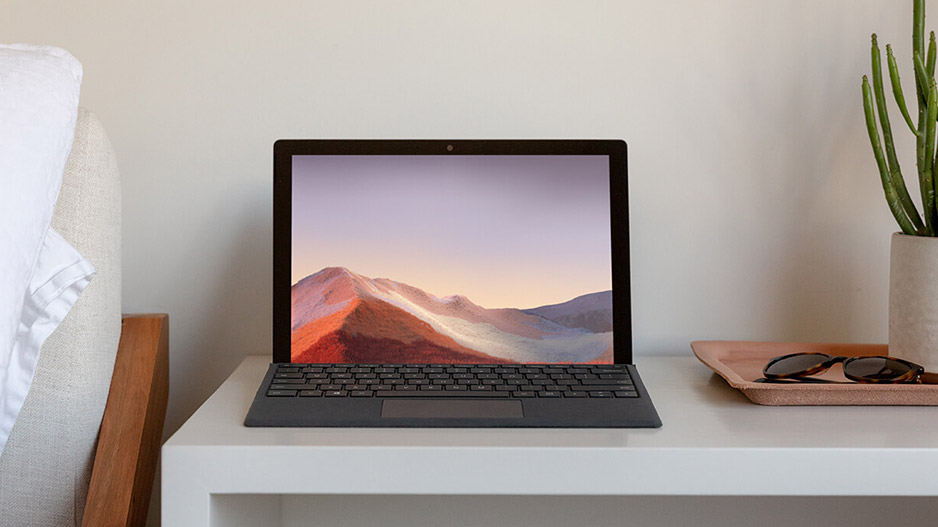 床边的桌子上有一台打开的 Surface Pro 7，附有黑色键盘盖